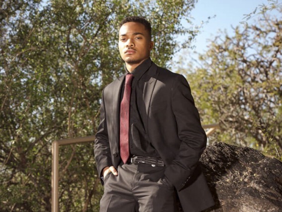 student worker standing the landscape wearing a black suit with a red tie